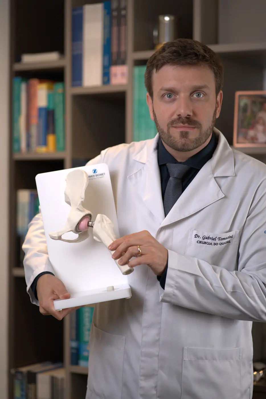 Dr. Gabriel Tomazini segurando um modelo demonstrativo de prótese de quadril